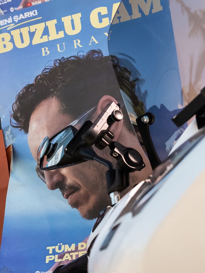Street coincidences captured in a poster reflected on a motorcycle mirror creating a witty visual effect.