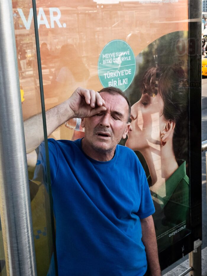 Man in blue shirt appearing to wipe his eye, aligned with a kissing woman on a street coincidence advertisement poster.