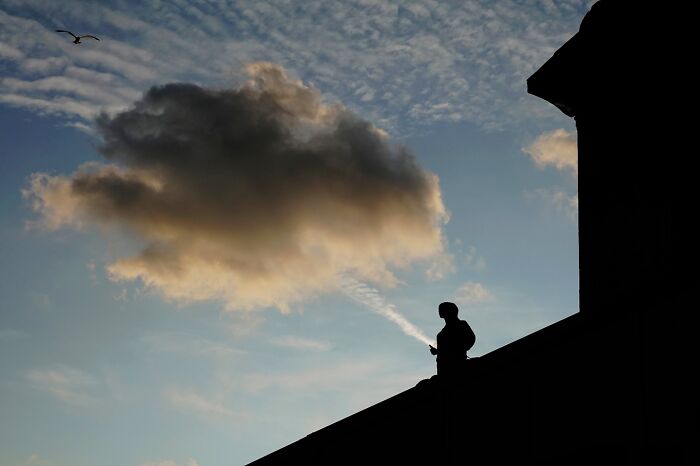 Silhouette of a person on rooftop blending with cloud formation, a captivating street coincidence captured in urban setting.