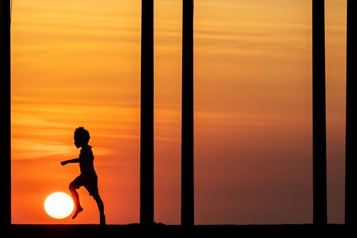 Silhouette of a child appearing to kick the sun during a colorful sunset, showcasing captivating street coincidences.