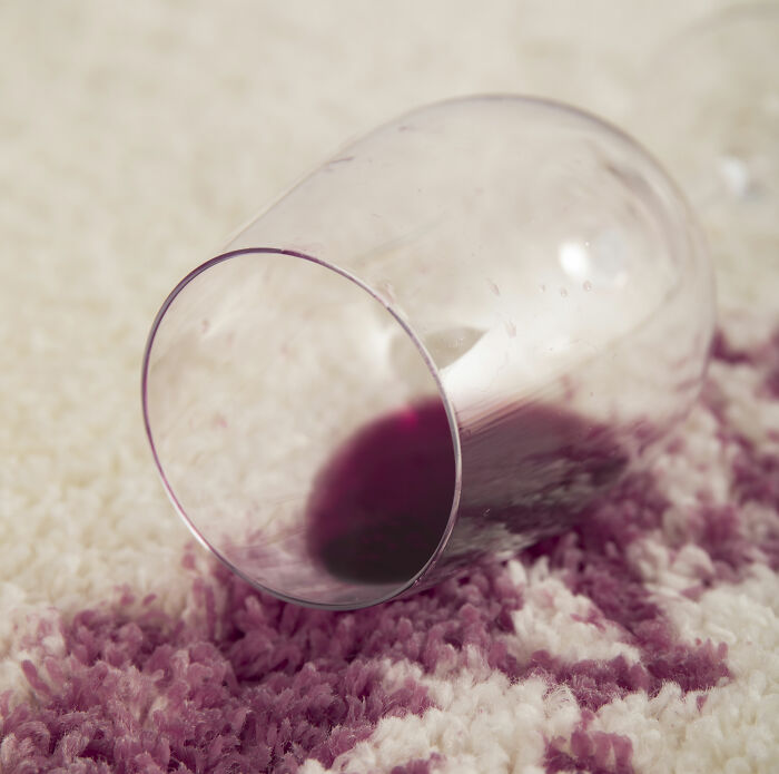 Spilled red wine on carpet from tipped glass, illustrating living next to horrible people and frustrating neighbor experiences.
