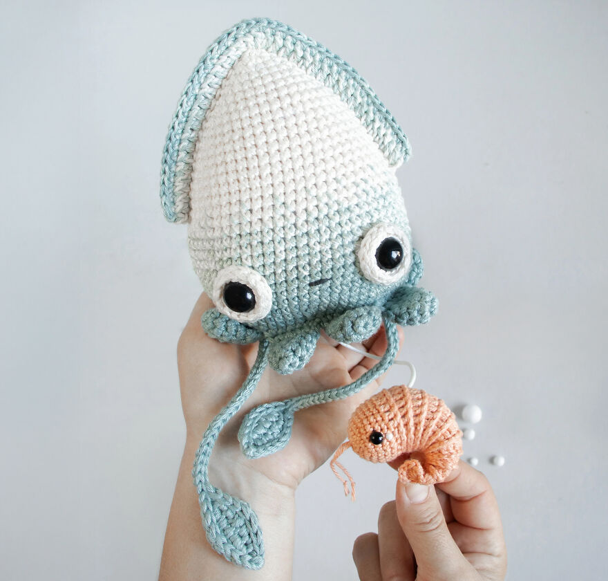Crochet animals with personality featuring a blue and white squid and a small orange shrimp held by hands.