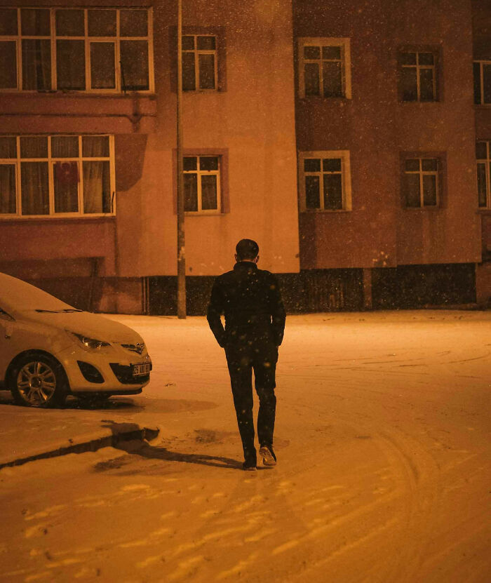 A person walking alone in a snowy residential area at night, illustrating living next to horrible people experience.