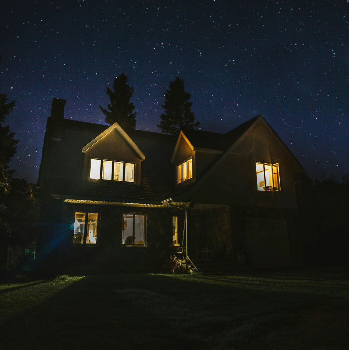 House lit up at night under a starry sky, illustrating a story about people living next to horrible neighbors.