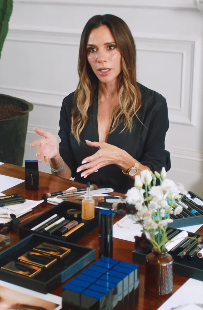 Victoria Beckham discussing her decision to ditch breast implants after the Spice Girls era, seated at a table with makeup.