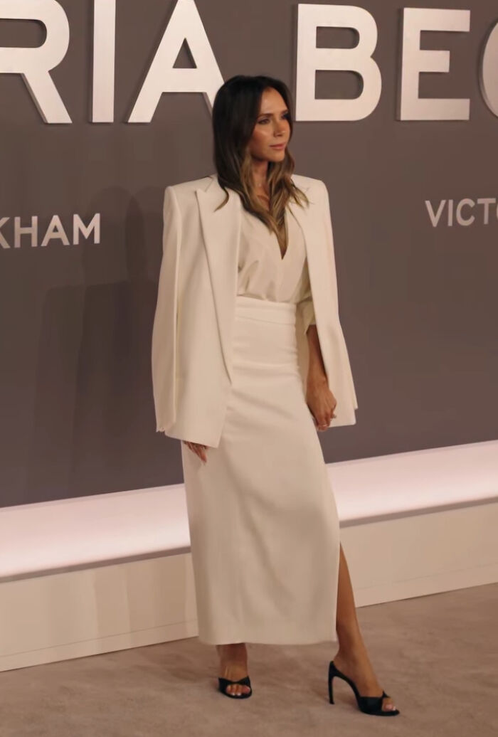 Victoria Beckham at a fashion event wearing an elegant white outfit after deciding to ditch her breast implants.