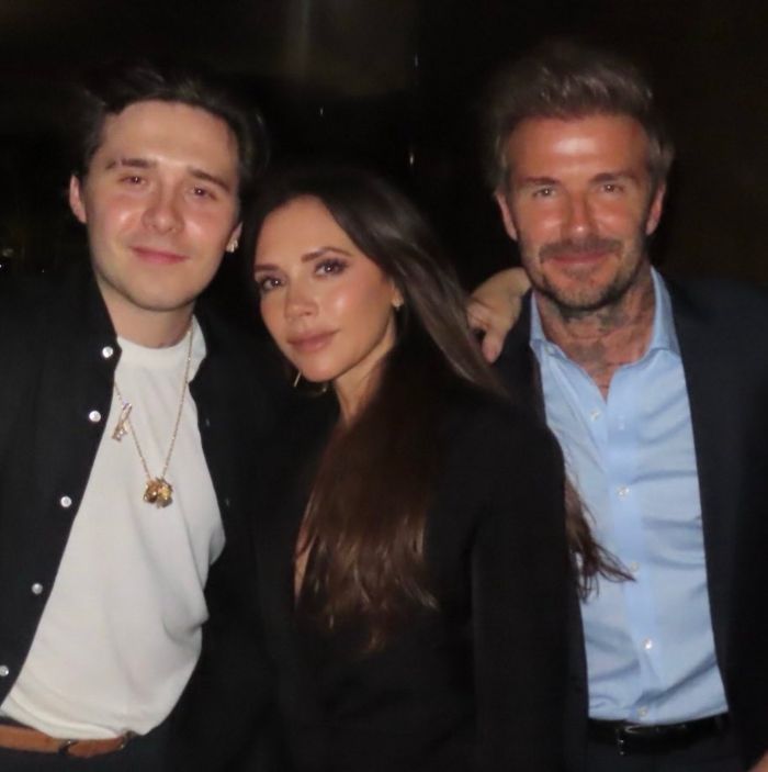 Victoria Beckham posing with two men at a nighttime event, highlighting her decision to ditch breast implants after Spice Girls.