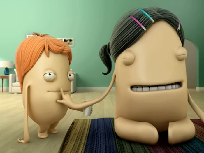 Two creepy animated characters in a living room scene, one touching the other's mouth in a surreal commercial setting.