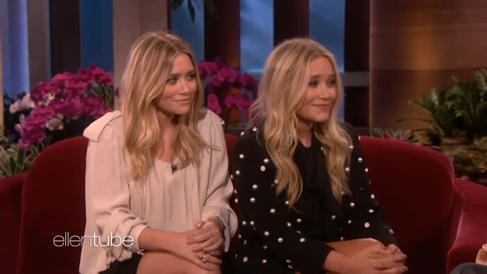 Celebrity twins sitting together on a talk show set, smiling and engaging in a lively conversation.