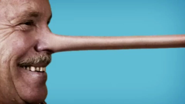 Close-up of a man smiling with an unnaturally long Pinocchio-style nose against a plain blue background, creepy commercial concept.