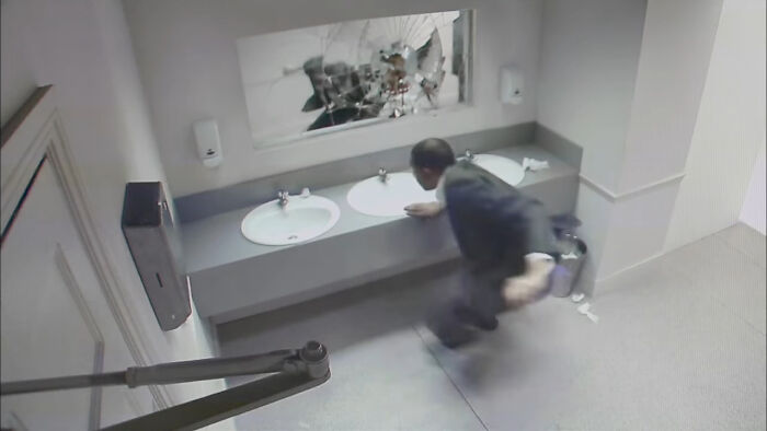 Man in a suit startled in a bathroom with a shattered mirror, evoking creepy commercial nightmare imagery.
