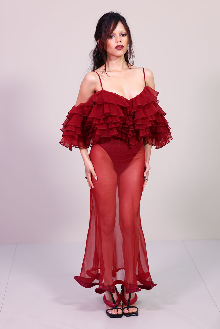 Model in a sheer red ruffled dress and black strappy heels showcasing a bold celebrity look at Paris Fashion Week 2025.