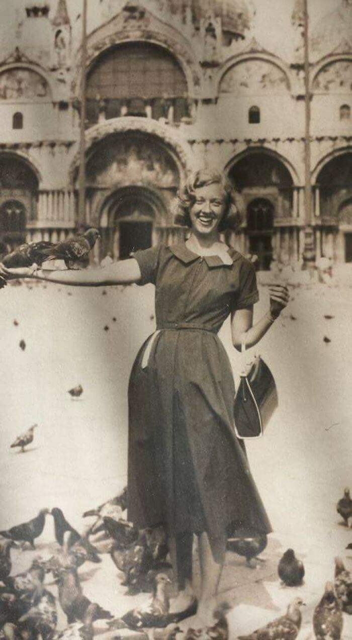 Vintage vacation photo of a smiling woman feeding pigeons in front of historic architecture before cell phones had cameras