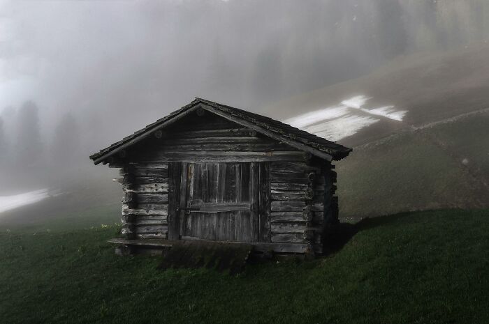 Creepy wooden cabin on foggy hillside setting a spooky scene for Halloween-inspired would you rather poll.