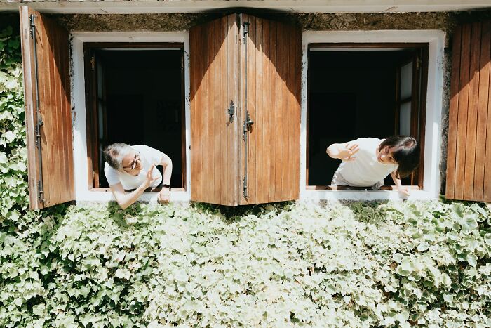 Two people leaning out of wooden windows surrounded by green ivy, illustrating subtle everyday sexism for men.