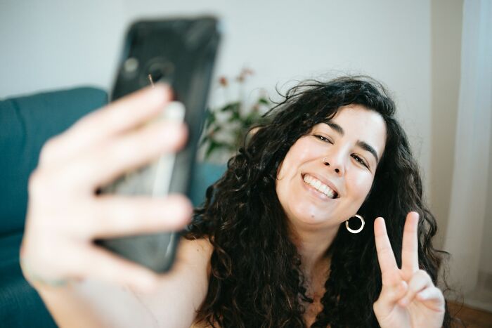 Young woman with curly hair taking a selfie at home.