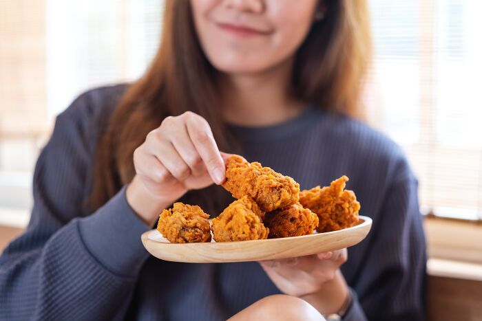 Woman holding a plate of fried chicken, enjoying a casual moment that fits the theme of drunk fumbles and bad decisions.