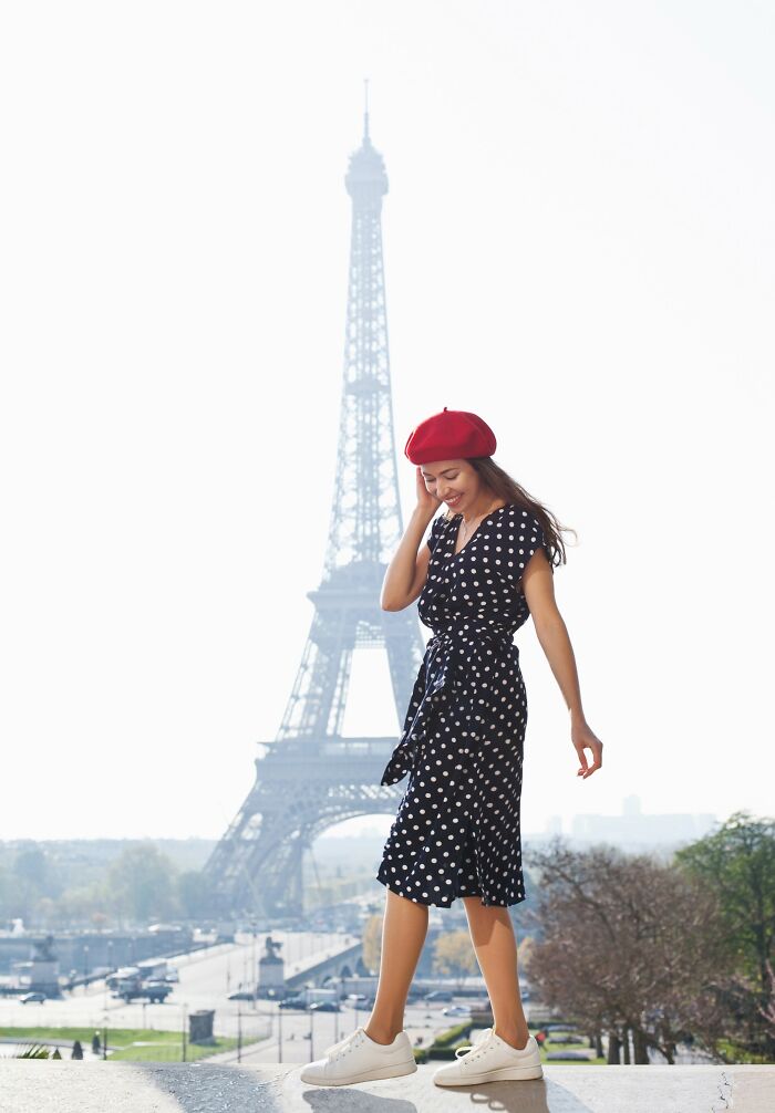 Woman in a red beret and polka dot dress near Eiffel Tower, illustrating positive stereotypes about various countries.