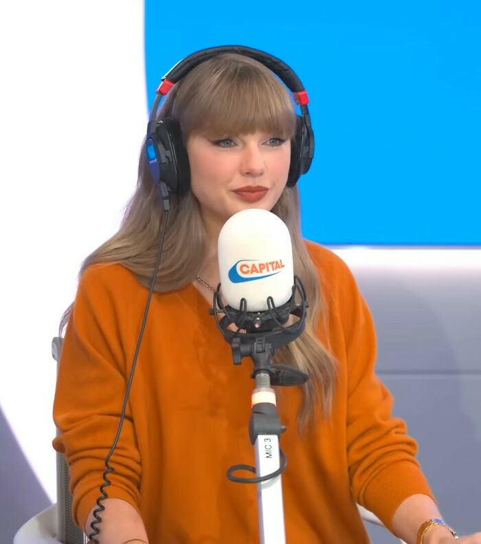 Taylor Swift wearing headphones and orange sweater during radio interview, drawing reactions about Caitlyn Jenner look.