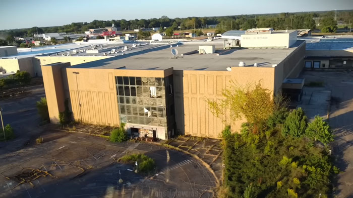 Abandoned ghost mall exterior with overgrown vegetation, focusing on urban explorers rescuing a trapped dog with a new leash.