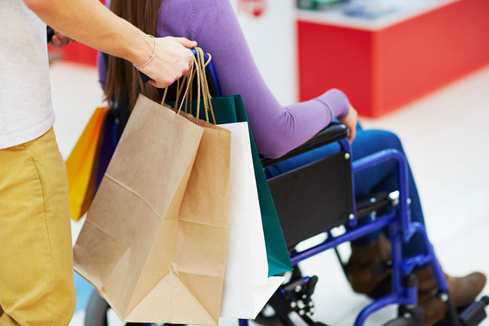 Teen in wheelchair shopping with friend carrying multiple bags, highlighting challenges faced by disabled teens in daily life.