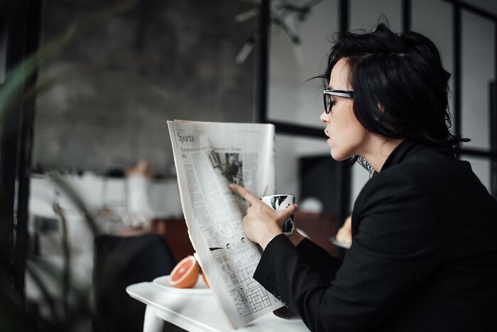 Person in glasses reading a newspaper and holding a cup, reflecting on experiences of losing jobs to AI technology.