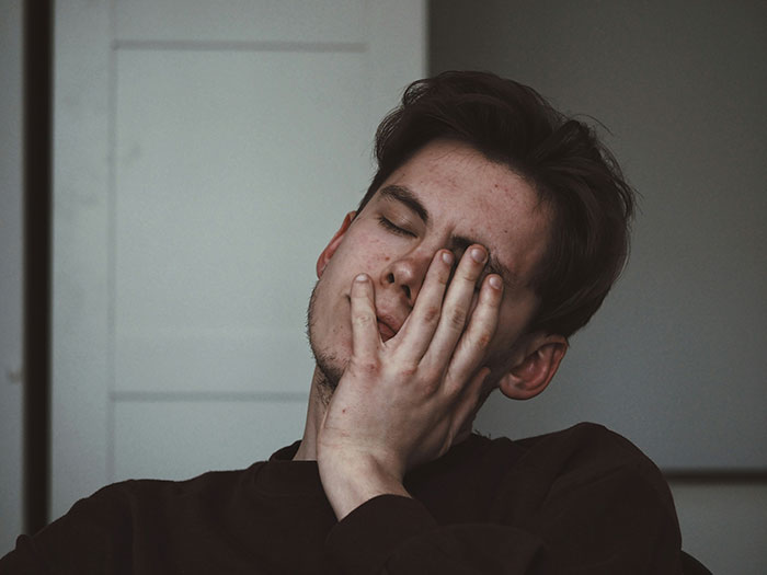 Young man with closed eyes, resting face on hand, conveying emotions related to rejection and dating after rejection.