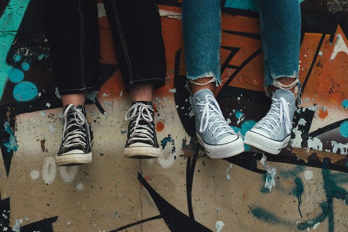 Two people wearing worn sneakers and jeans sit against a colorful graffiti wall.