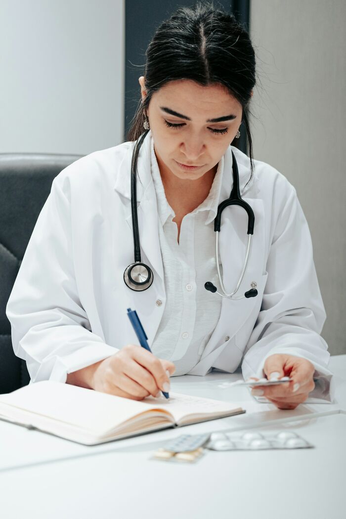 Female doctor with stethoscope writing notes and examining medication, highlighting serious medical problems concept