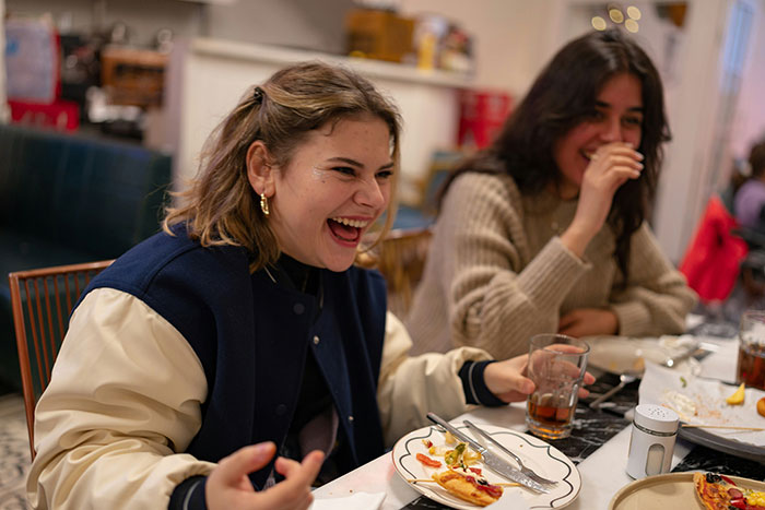 Two women laughing at a restaurant table, illustrating a roast and emotional reactions over raisin potatoes.