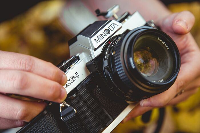 Close-up of hands adjusting settings on a Minolta camera, illustrating moments wedding guests made the bride and groom regret.