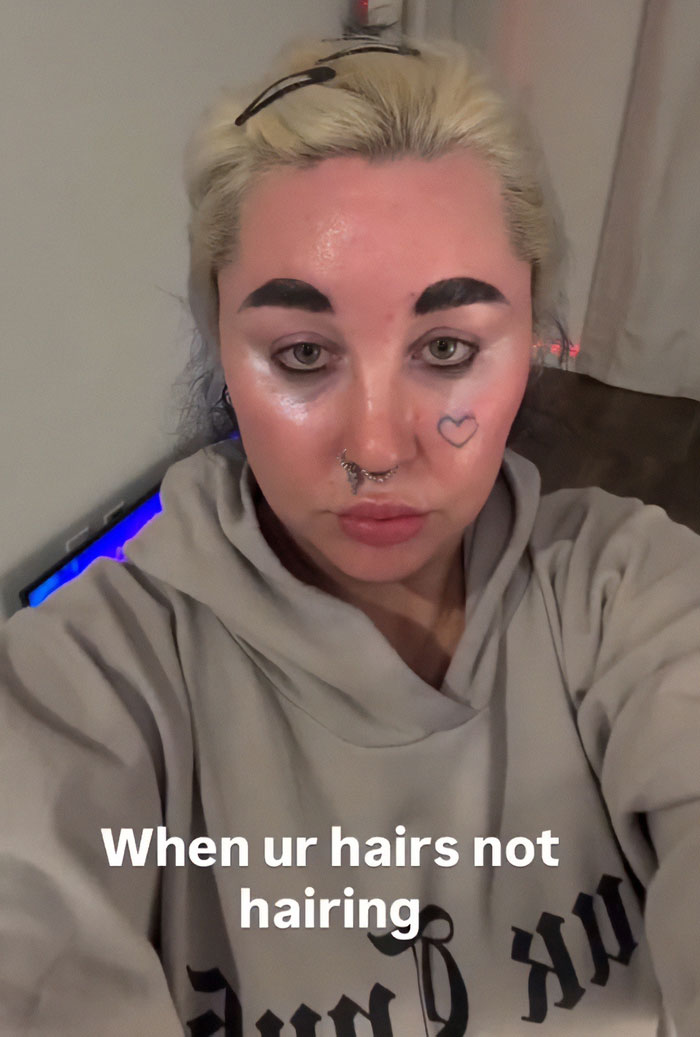 Amanda Bynes showing unrecognizable look with heart face tattoo and bold eyebrows in casual hoodie indoors.