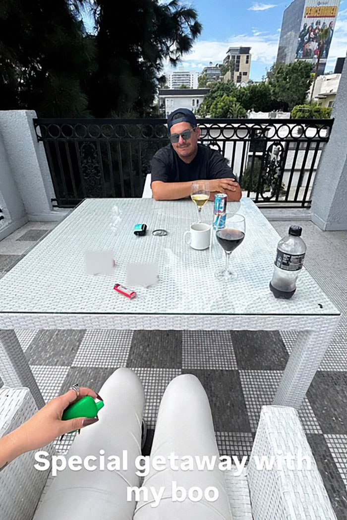 Man sitting at outdoor patio table during daytime hinting at new romance with mystery man after unrecognizable look debut