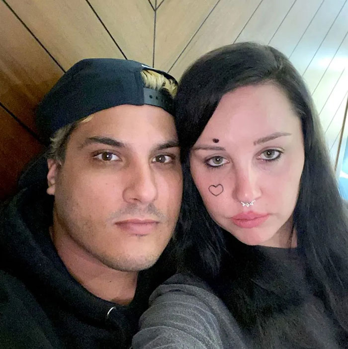 Amanda Bynes with a new look posing closely with a mystery man in a casual indoor setting.