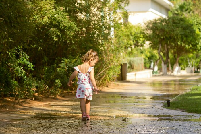 Toddler girl walking alone on a sunlit path, surrounded by greenery, illustrating subtle everyday sexism in society.