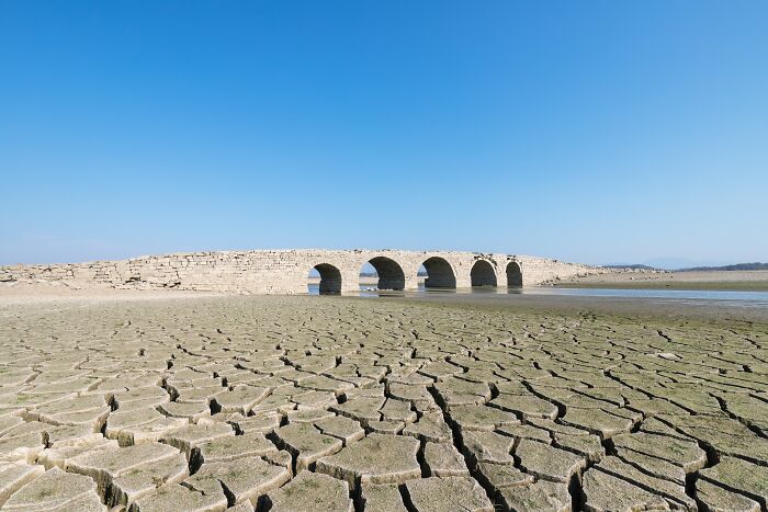 Ancient stone bridge over dried c*****d earth under clear blue sky showing unbelievable facts about countries.