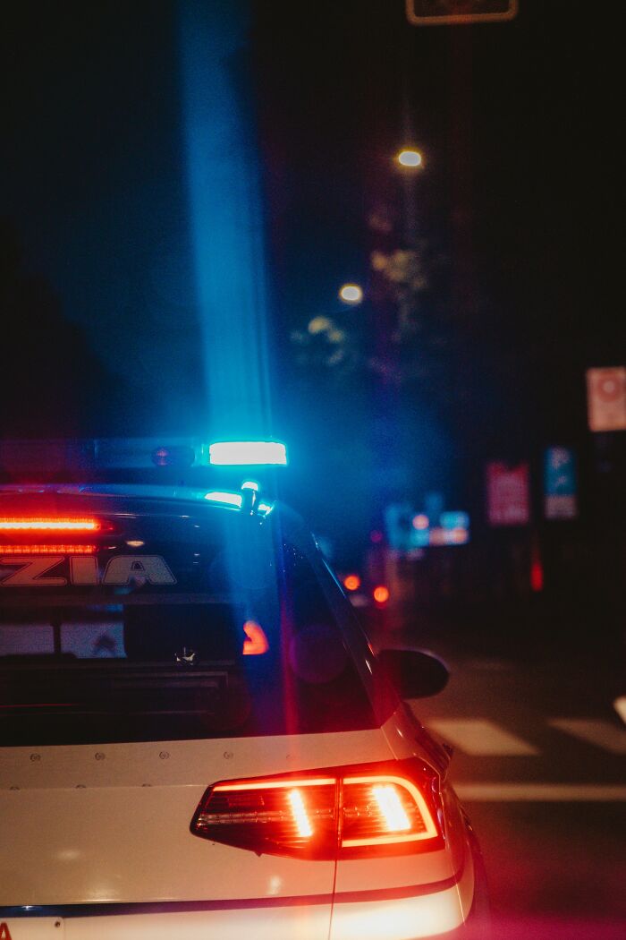 Police car with emergency lights flashing at night on a dark street, symbolizing karma striking with zero mercy.