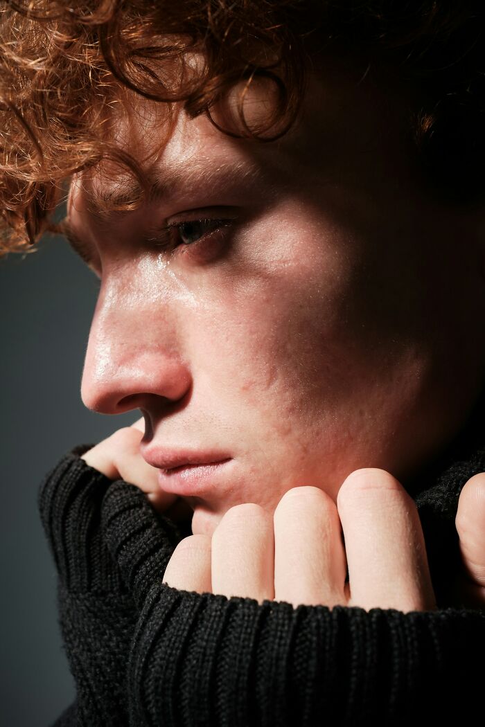 Young person with curly hair crying and holding black sweater collar, reflecting on funeral stories and emotions.
