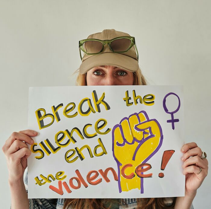 Person holding a sign reading break the silence end the violence with a raised fist and female gender symbol.