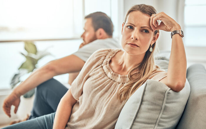Woman looking concerned on couch while man sits back-to-back, highlighting Annexe Son House family relationship tension.