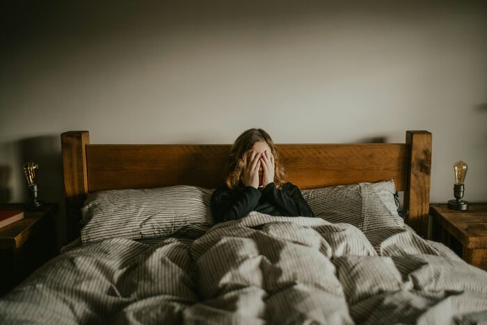 Person sitting in bed covering their face, illustrating moments when the universe had their back and protected them from harm.