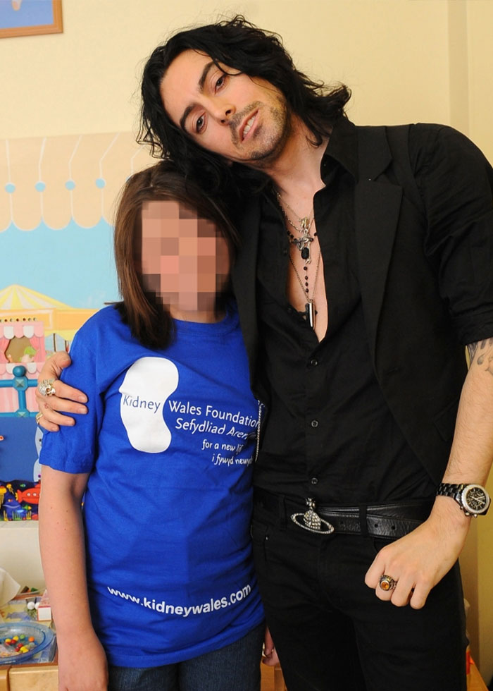 Rock star posing with a young fan indoors wearing a blue Kidney Wales Foundation t-shirt.