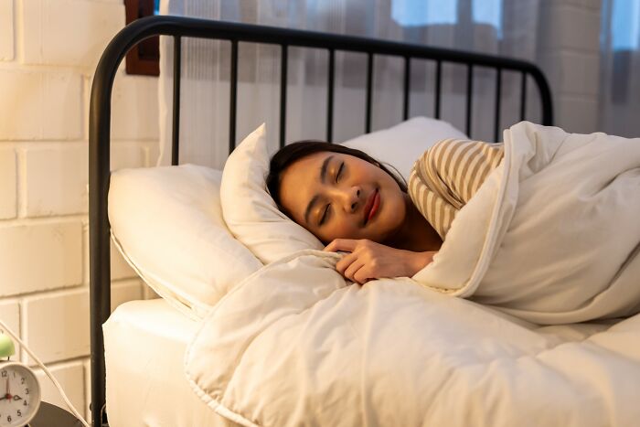 Young woman peacefully sleeping in bed wrapped in a blanket after recovering from drunk fumbles and bad decisions.