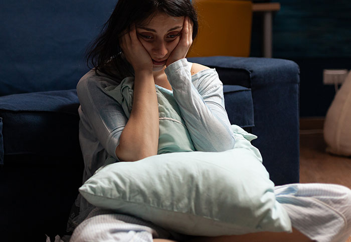 Woman sitting on the floor looking stressed, holding a pillow, upset about roommate paying more for new couch.