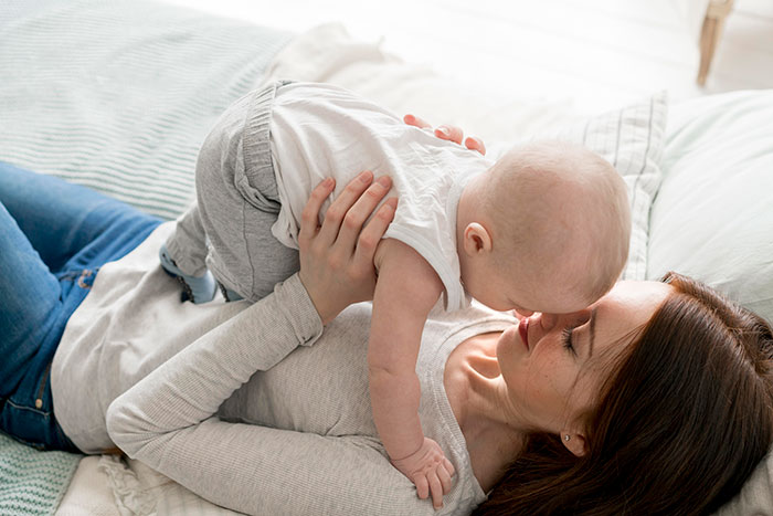 Mother lying on bed holding newborn baby above her face, highlighting newborn care and family bonding moments.