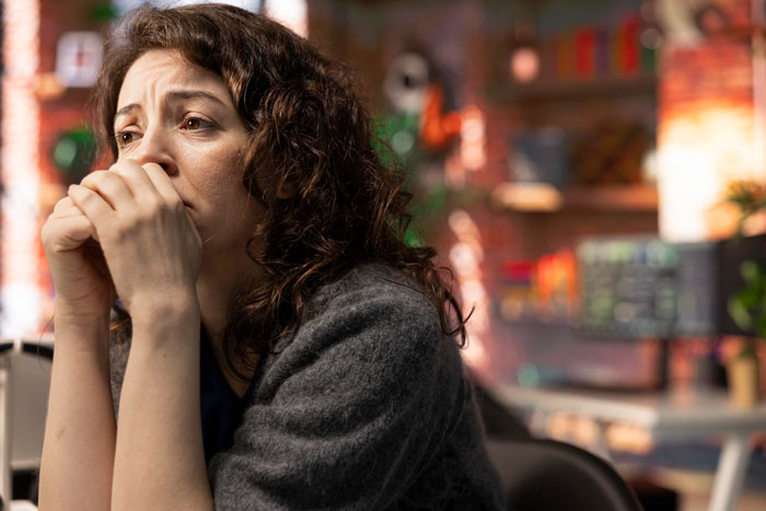 Woman with curly hair having a panic attack at a restaurant, visibly upset and distressed while waiting for food.