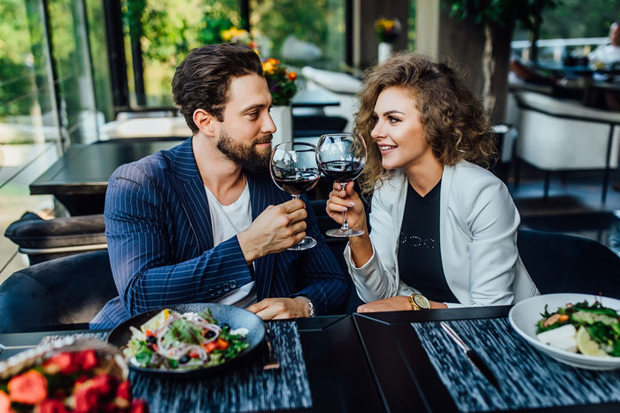 Couple enjoying wine and salad at a modern restaurant, sharing a cheerful moment in a bright dining area.