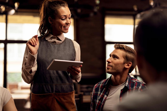 Waitress smiling and taking order on tablet from a customer in a restaurant setting, highlighting autistic woman panic attack.