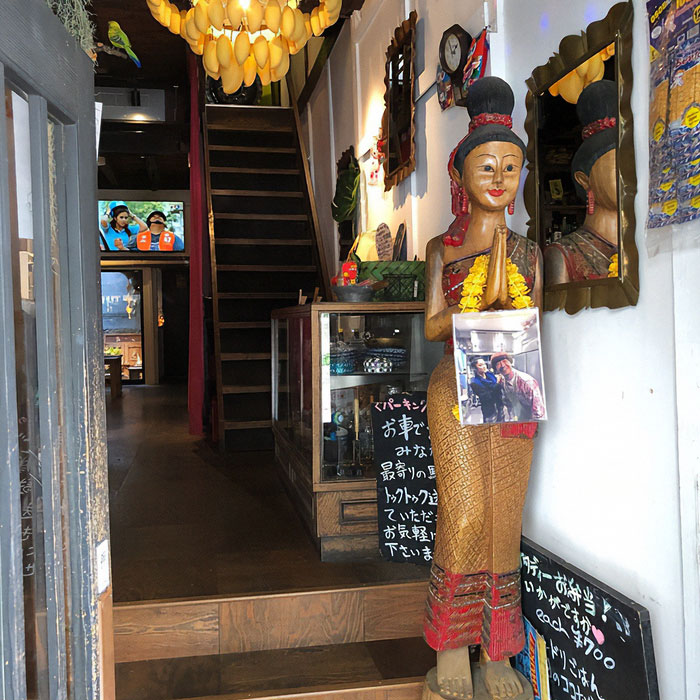 Entrance of a Japanese restaurant featuring a traditional wooden statue, sparking debate over tourists' revealing sports attire. Entrance of a Japanese restaurant featuring a traditional wooden statue, sparking debate over tourists' revealing sports attire.