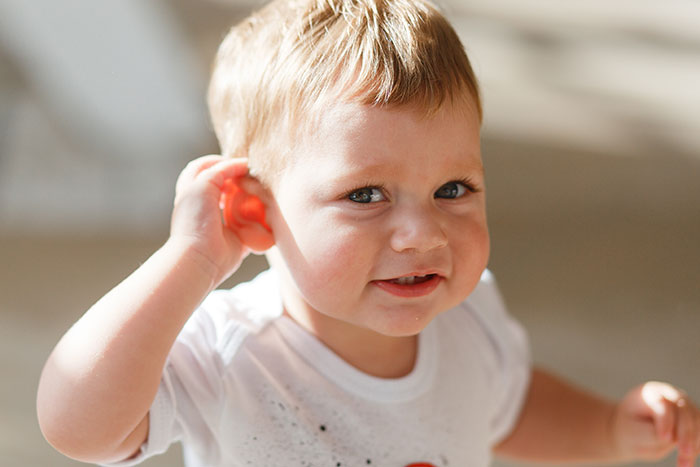 Toddler boy with blonde hair playing indoors, symbolizing sibling of autistic and epileptic brothers facing neglect challenges.